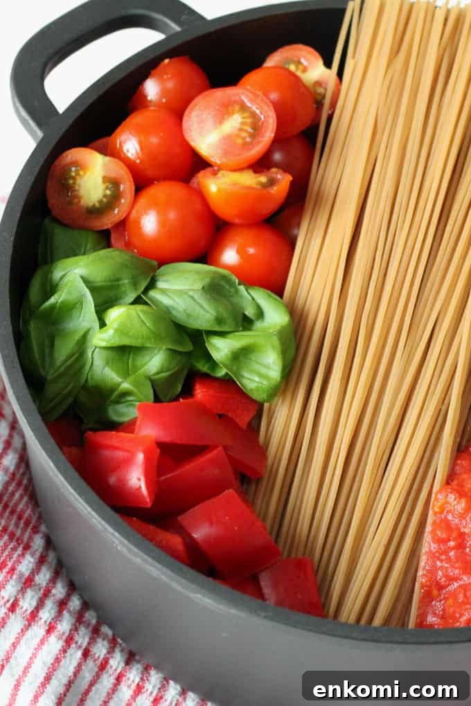 Creamy One-Pot Sausage and Tomato Spaghetti Recipe 4 chopped cherry tomatoes, fresh basil leaves, gluten free pasta and chopped red peppers in a black pot