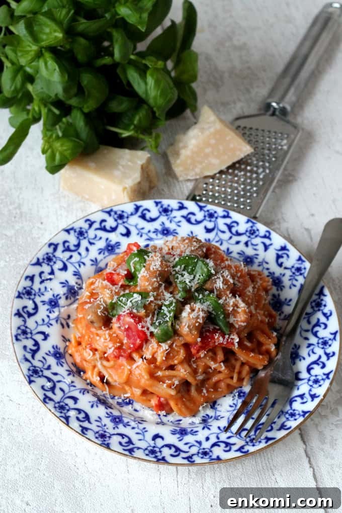 Creamy One-Pot Sausage and Tomato Spaghetti Recipe 6 One Pot Creamy Sausage & Tomato Spaghetti served on a blue and white plate with grated parmesan and basil leaves