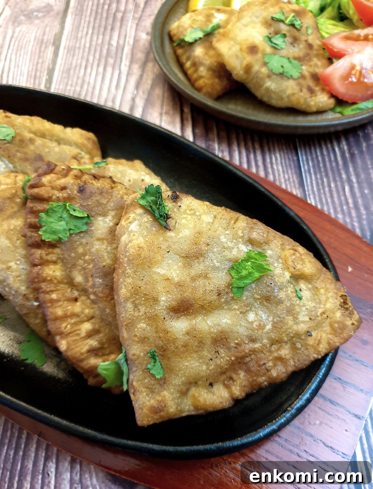 Crispy cheese and sweetcorn samosas on a black plate.