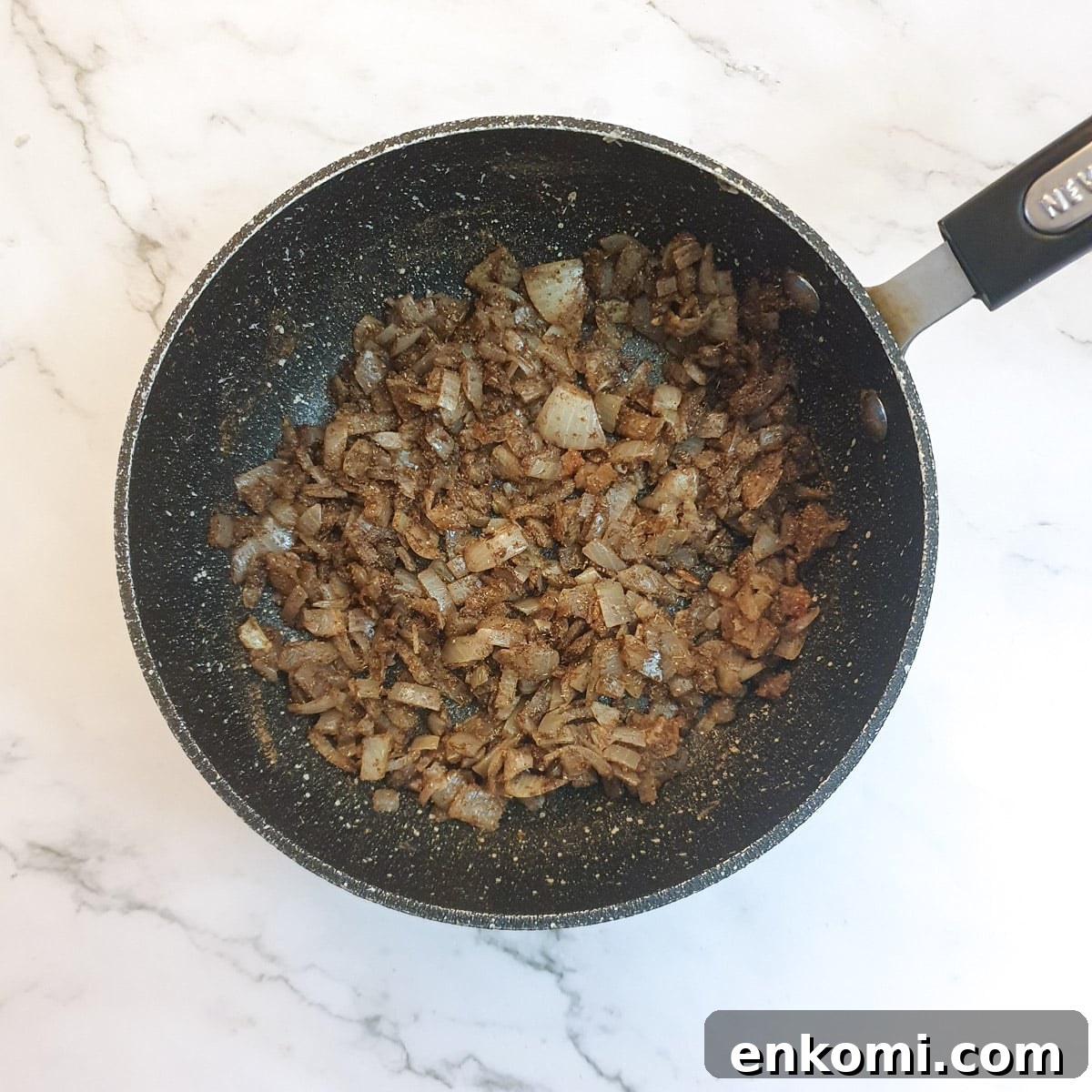 Spices added to onions in a frying pan.