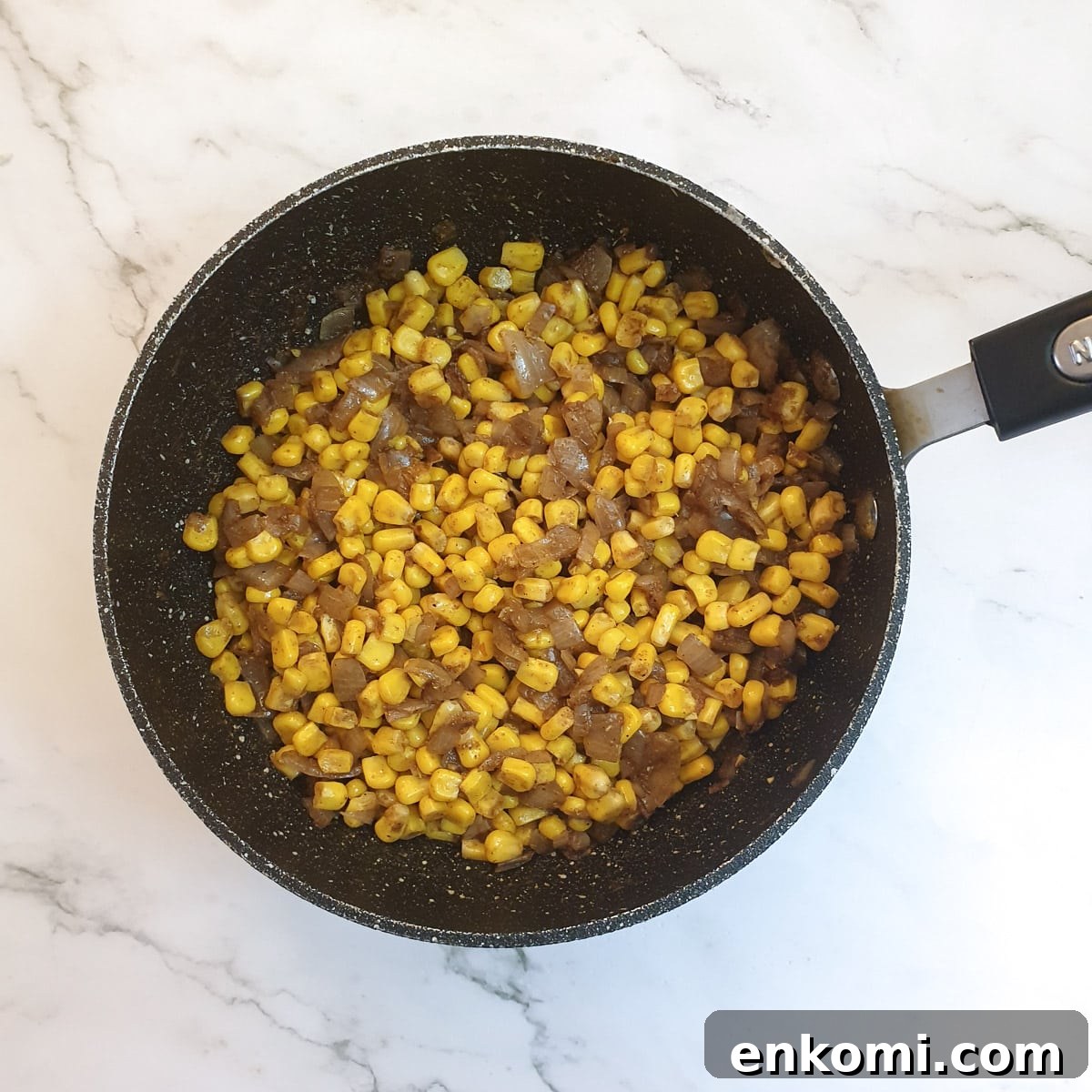 Canned sweetcorn mixed with onions and spices in a frying pan.