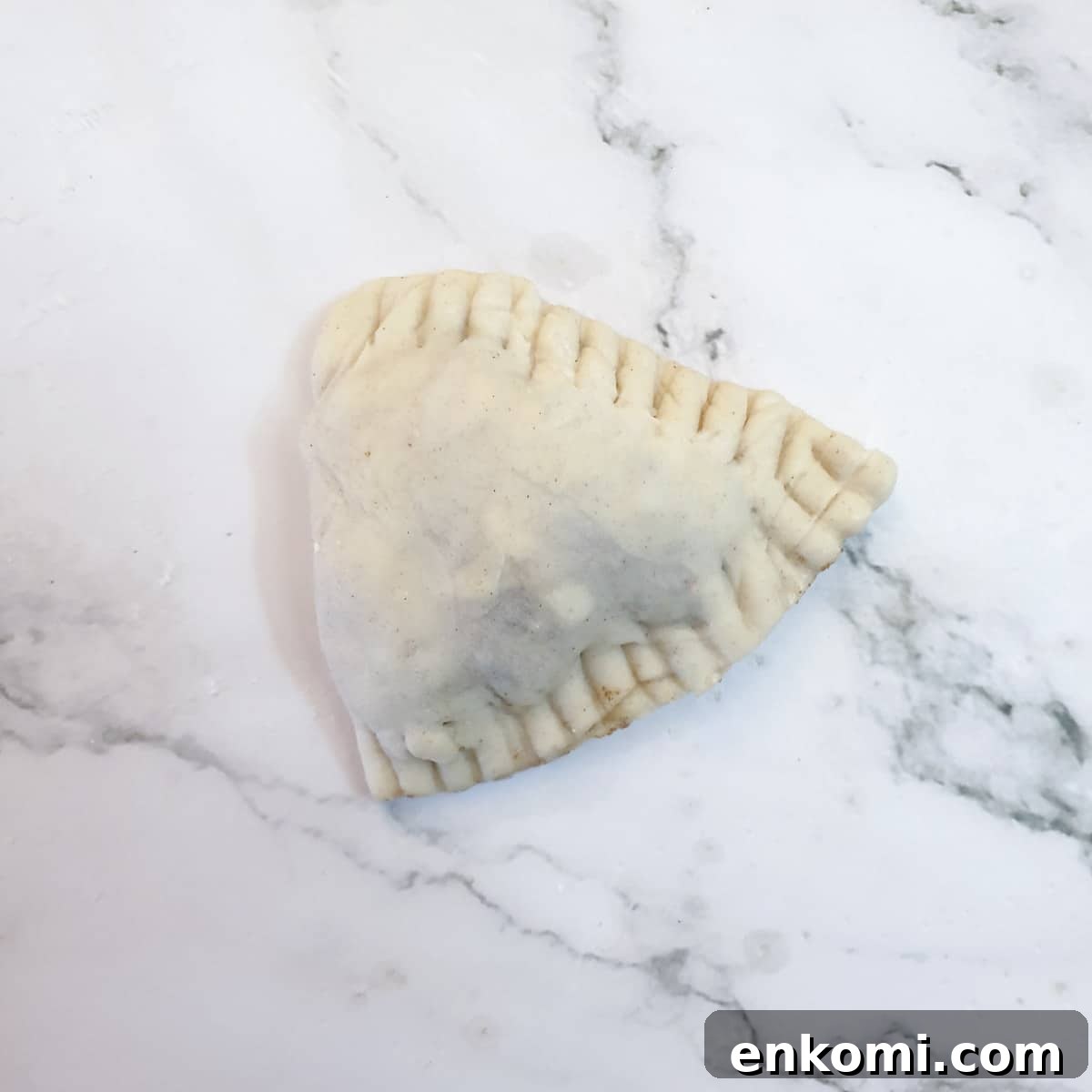 An unbaked cheese and sweetcorn samosa showing the crimped edges.