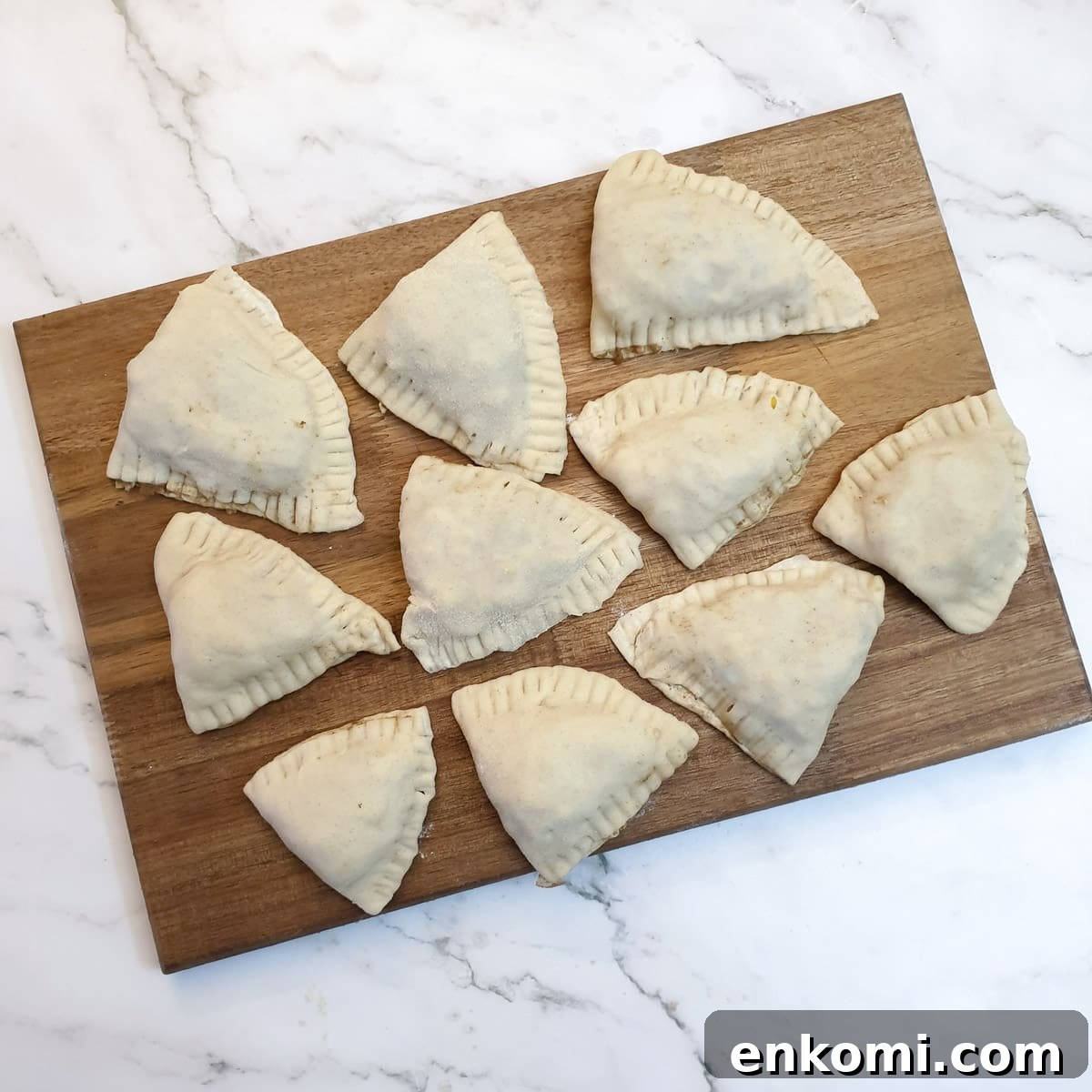 10 unbaked samosas on a wooden board.