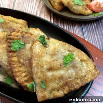 Crispy cheese and sweetcorn samosas on a black plate.