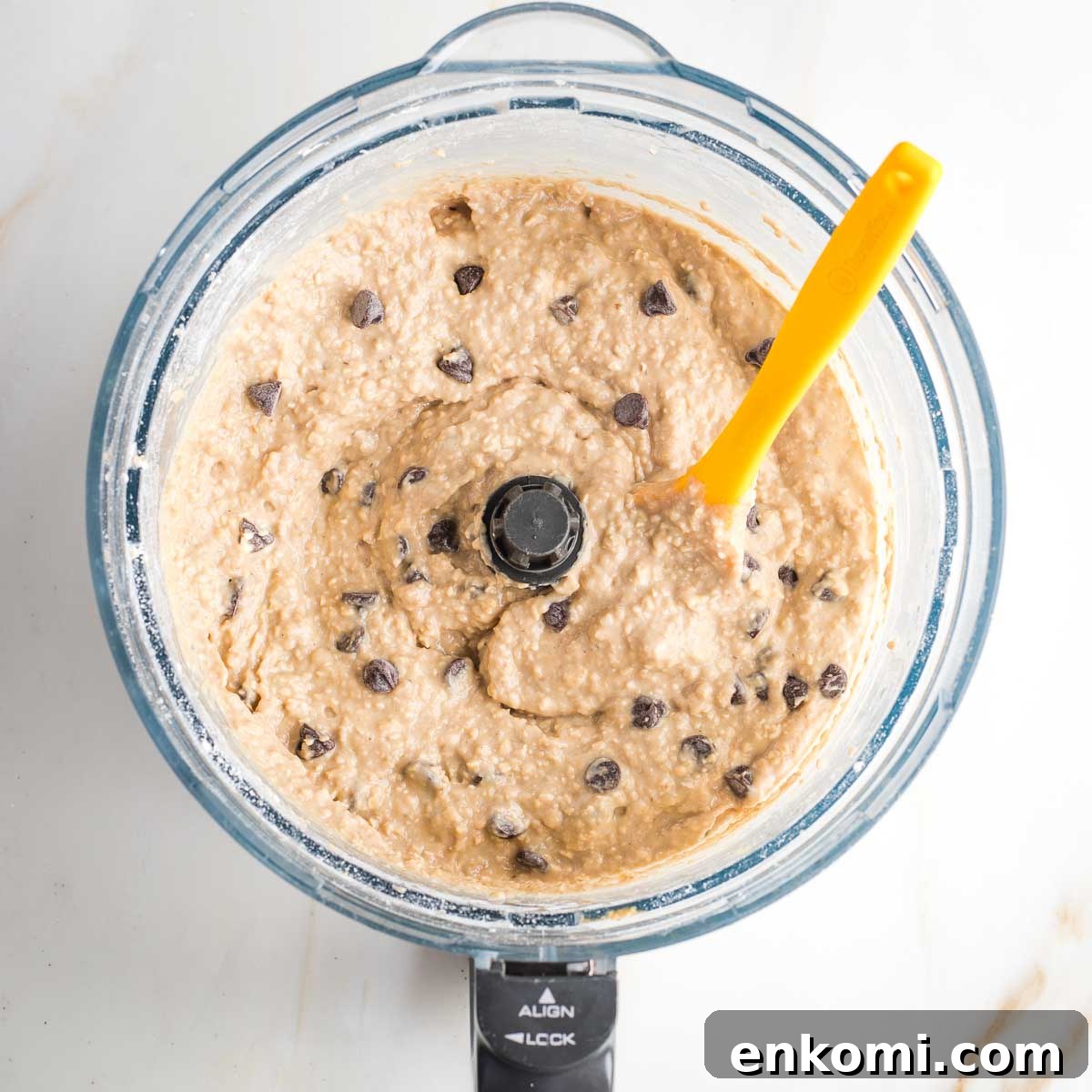 Spatula mixing chocolate chips into blondie batter in the bowl of a food processor. 