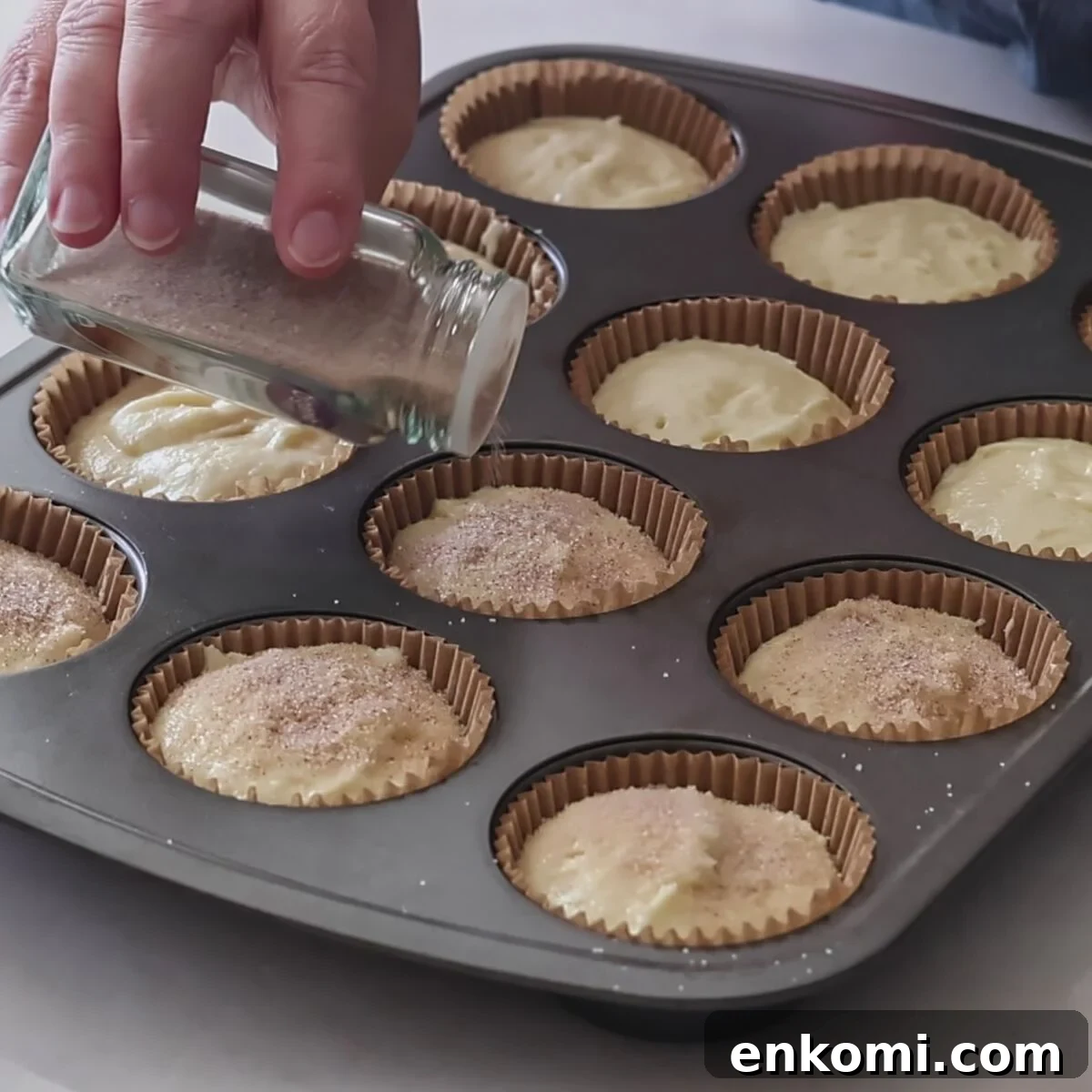 Gluten-Free Churro Cupcakes Recipe with Cinnamon Sugar Topping 11 sprinkling cinnamon and sugar on top of cupcake batter in muffin pan.