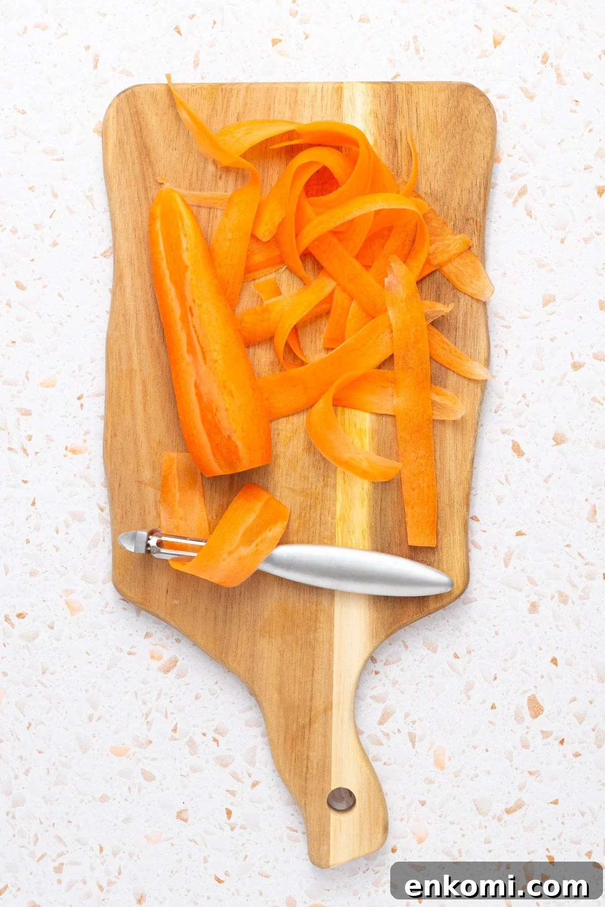 An overhead image of a carrot being peeled into thin ribbons on a chipping board.