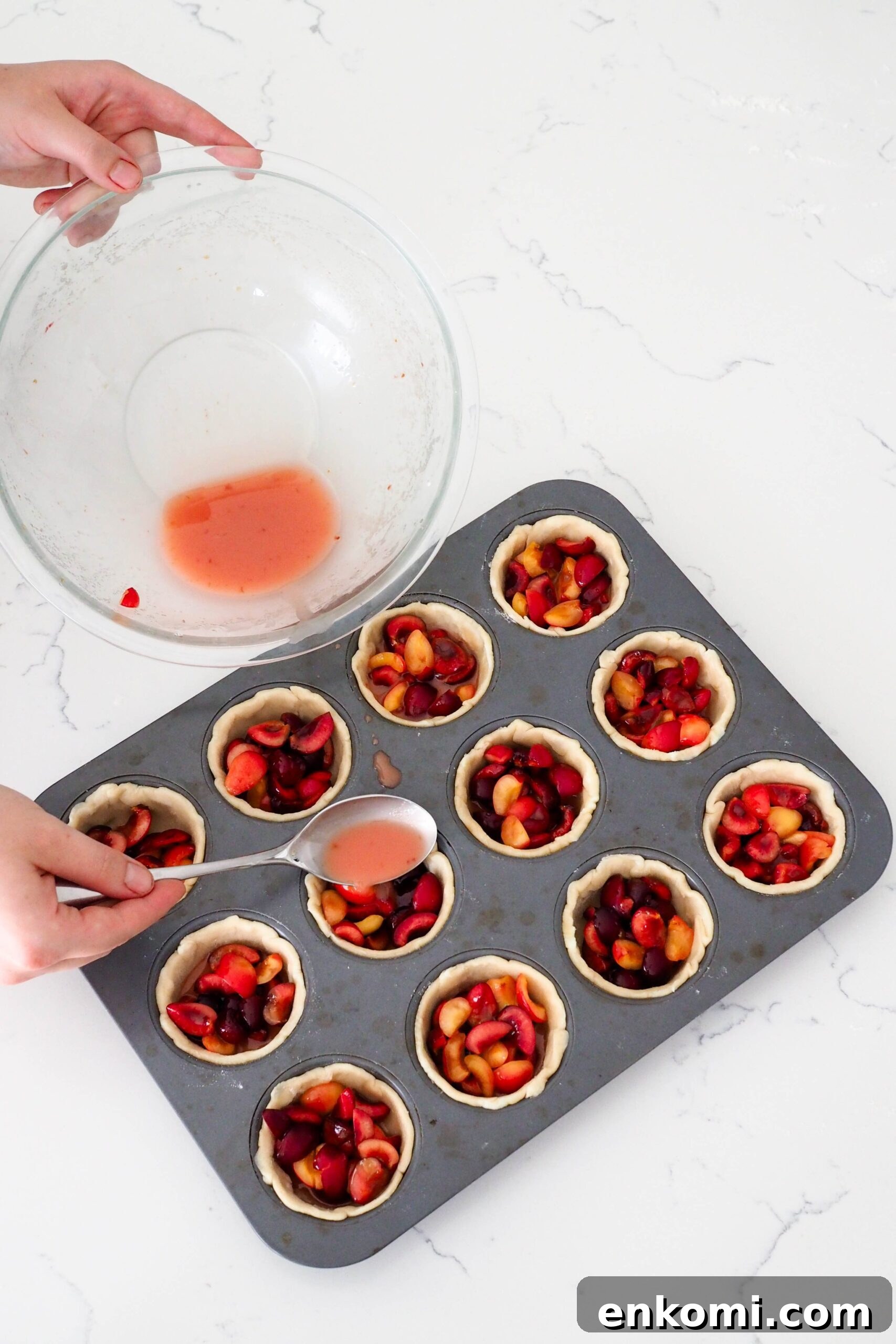 Mini Cherry Pies Recipe: Perfect Handheld Fruit Tarts 9 A hand uses a tablespoon to add pink liquid to mini cherry pies.