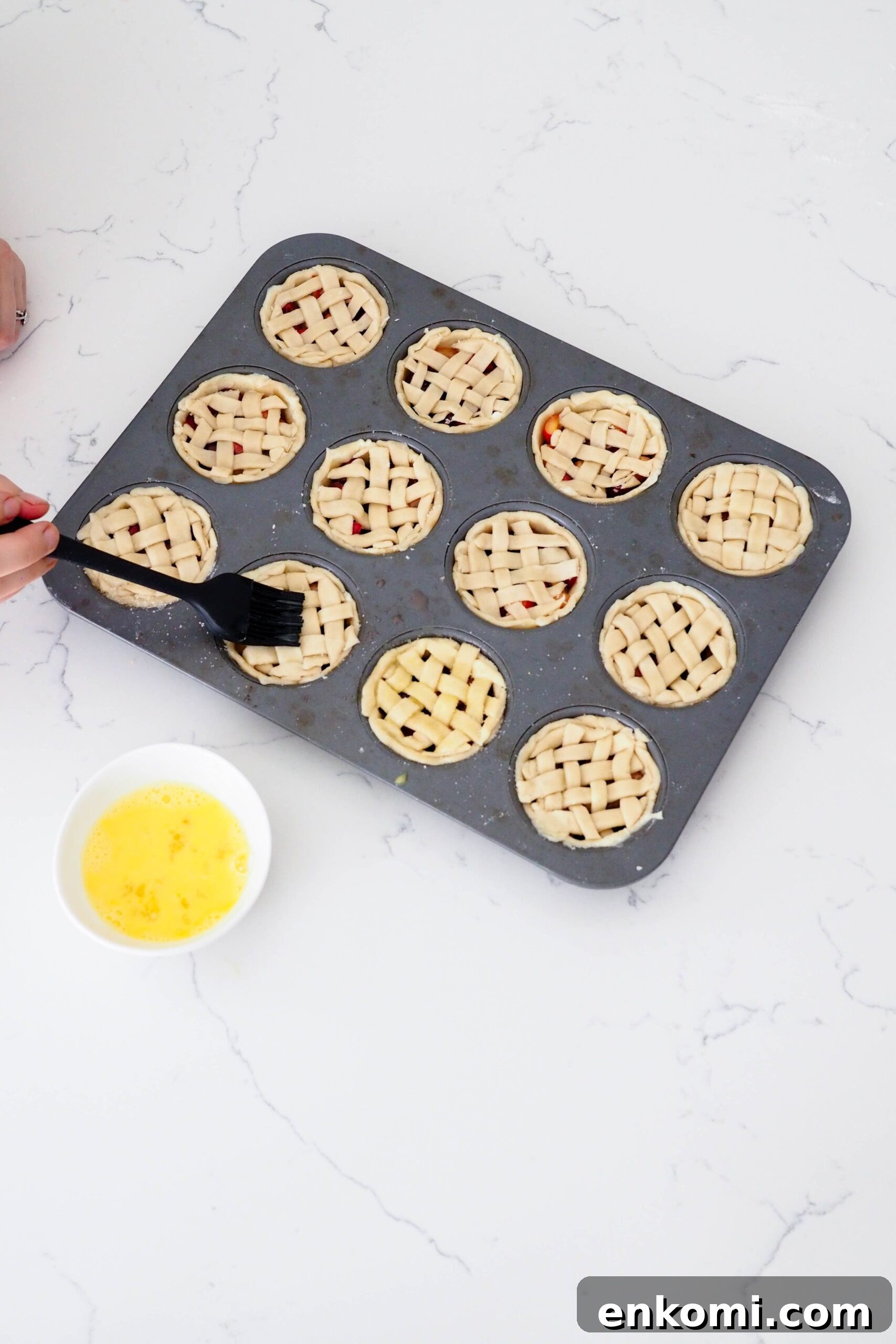 Mini Cherry Pies Recipe: Perfect Handheld Fruit Tarts 12 A hand uses a silicone pastry brush to brush egg wash onto mini latticed pies.