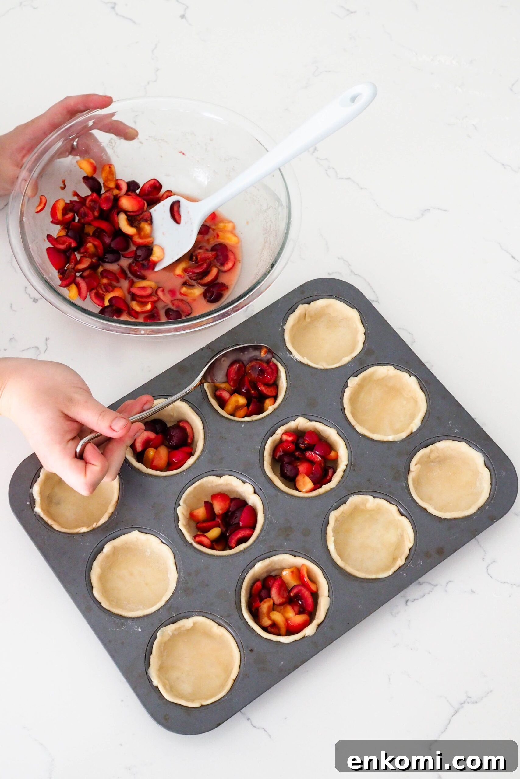 Mini Cherry Pies Recipe: Perfect Handheld Fruit Tarts 8 A hand uses a tablespoon to spoon cherries into mini pies.