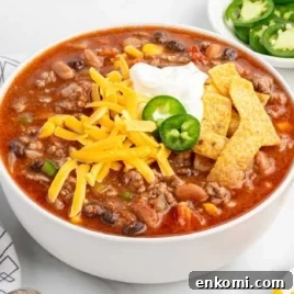 Overhead view of taco soup bowl with cheddar cheese, sour cream, jalapeño, and tortilla strips set against a background of the soup's surface.