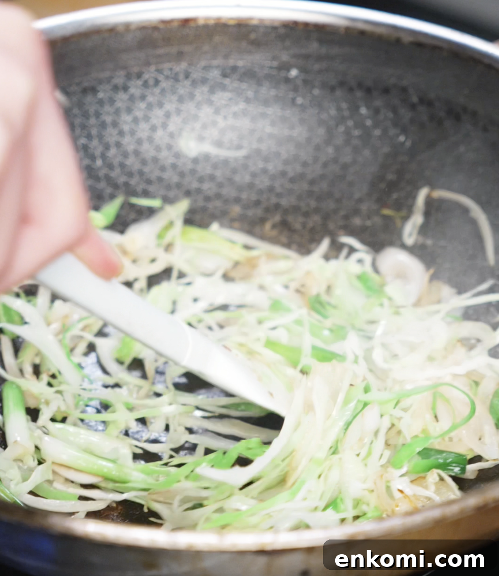 Crispy Chicken Pan-Fried Noodles with Garlic Scallions 8 Sliced onions and scallion whites are being sautéed in a wok. These vegetables create an aromatic base for the sauce to cling to later.
