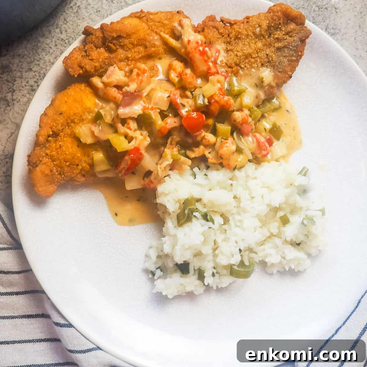 a white plate with fried catfish, crawfish etouffee, and green onion rice on it