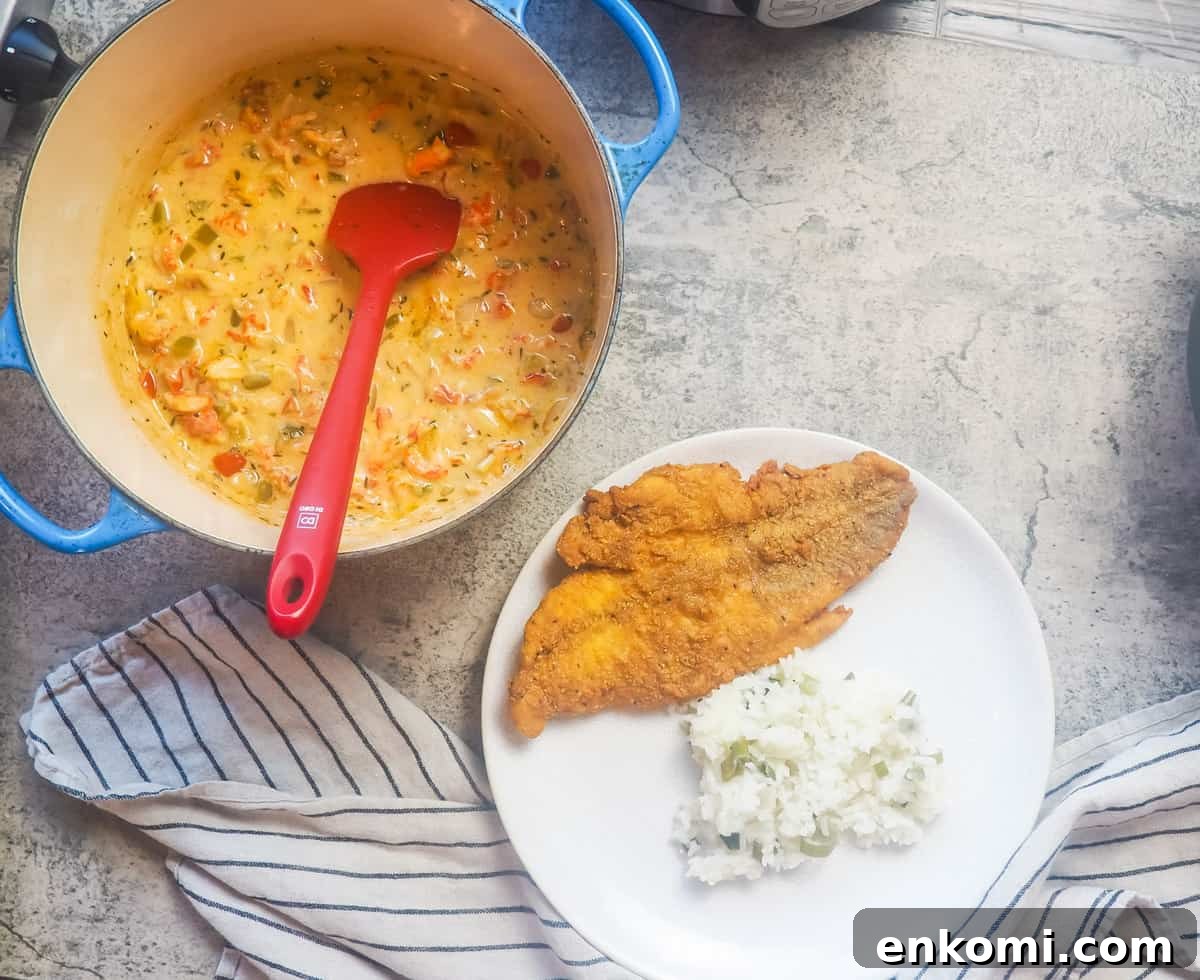 a white plate with fried catfish, crawfish etouffee, and green onion rice on it with a pot of crawfish etouffee