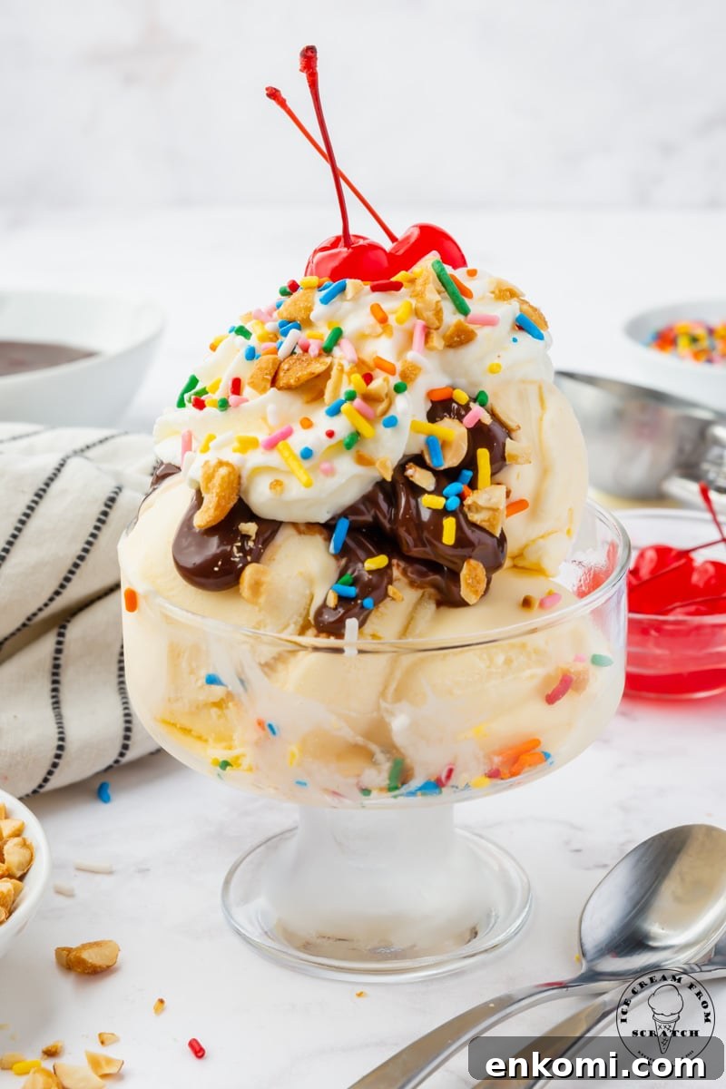 Decadent Hot Fudge Sundae Recipe You’ll Love 2 a clear footed ice cream dish filled with a hot fudge sundae topped with peanuts, whipped cream, sprinkles, and two stemmed cherries.