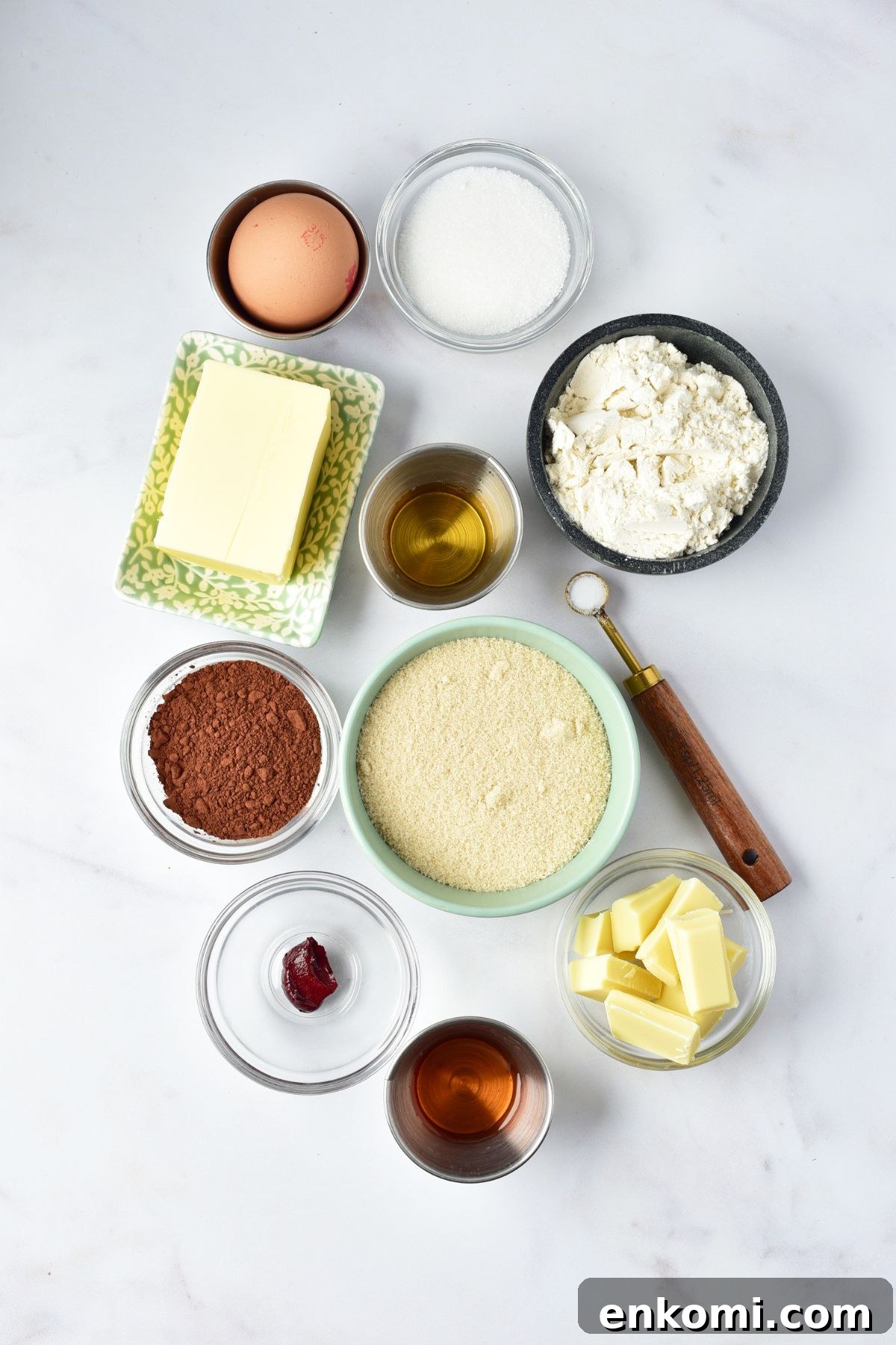 Ingredients needed to make red velvet brownies measured in small bowls on a white marble table. 
