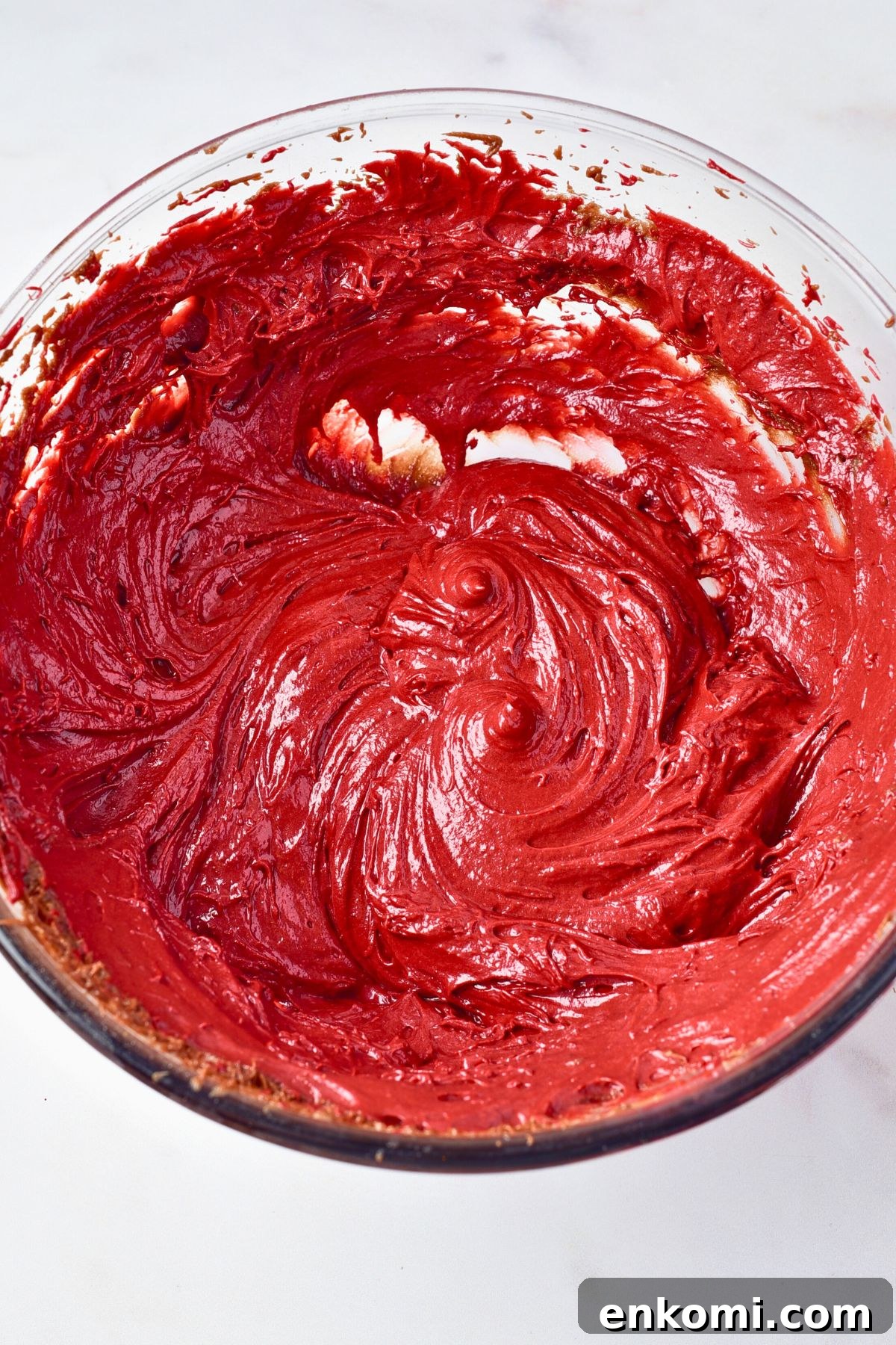 Bright red brownie batter in a clear glass bowl. 