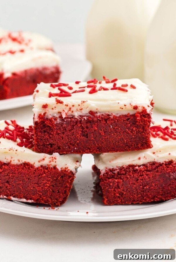 Red velvet bars frosted with cream cheese frosting, stacked on a white plate.