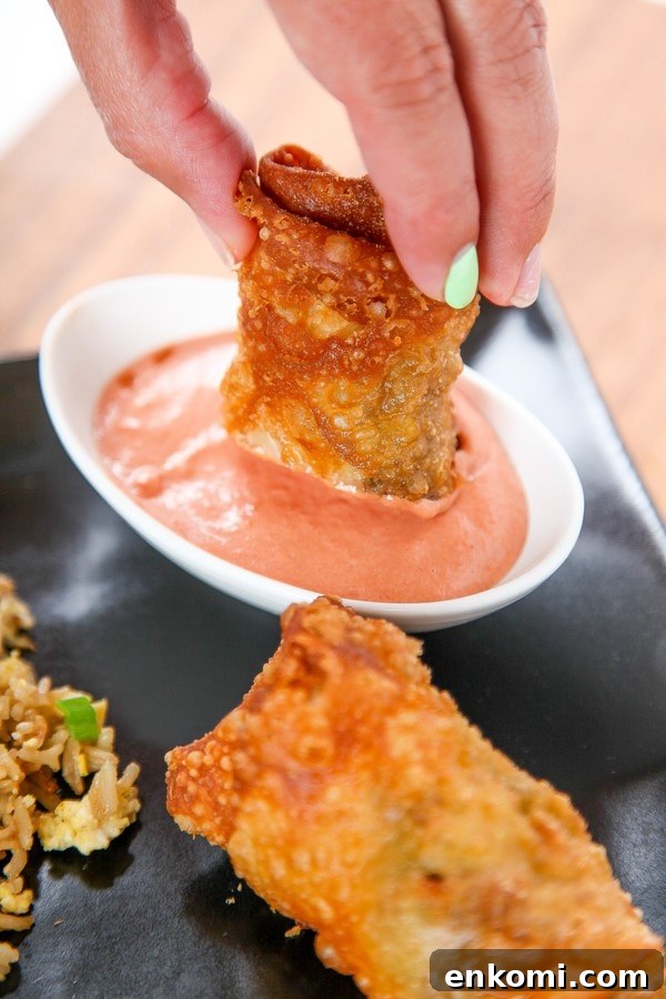 a cheeseburger egg roll being dipped into a ketchup and mayonnaise sauce. 