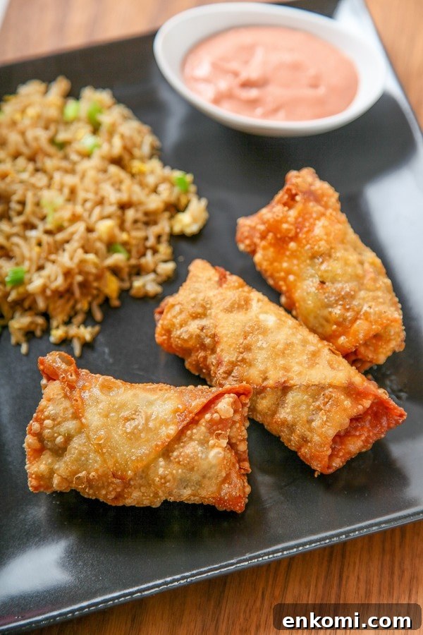 three cheeseburger egg rolls on a black plate with fried rice.
