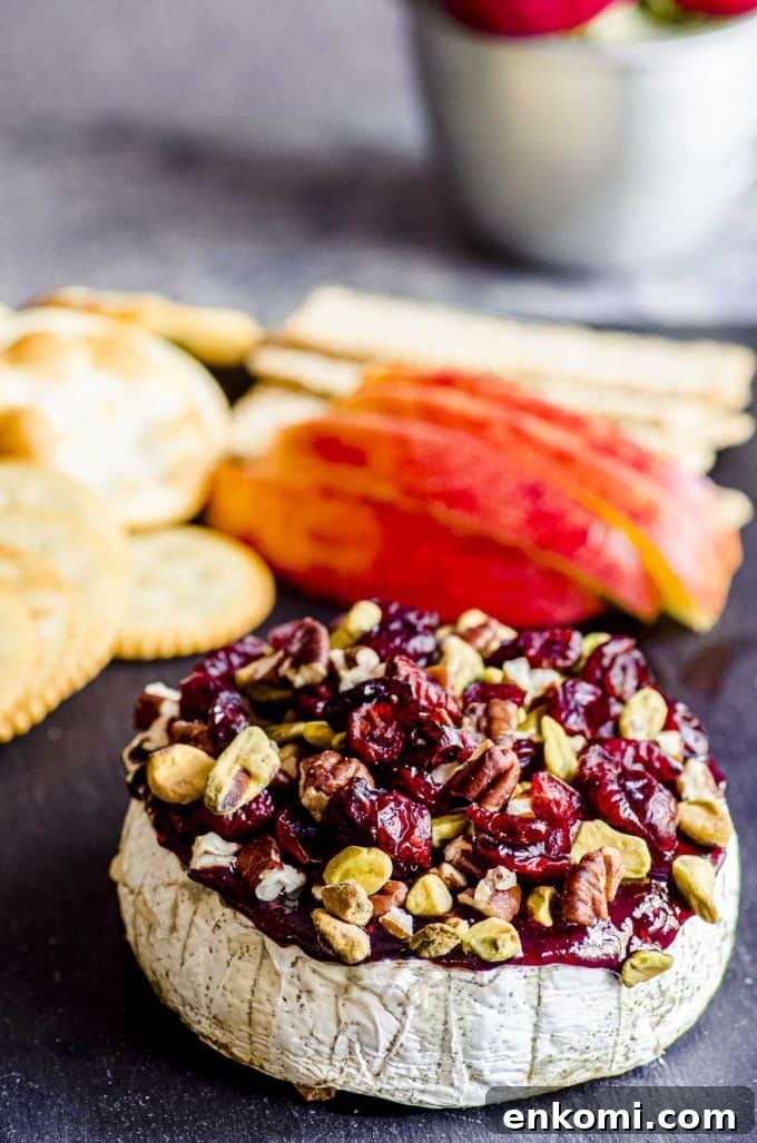 Cranberry Pecan Baked Brie: Warm Appetizer for Holiday Entertaining 2 An angled view of baked brie with apple slices and crackers behind it