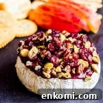 An angled view of baked brie with apple slices and crackers behind it