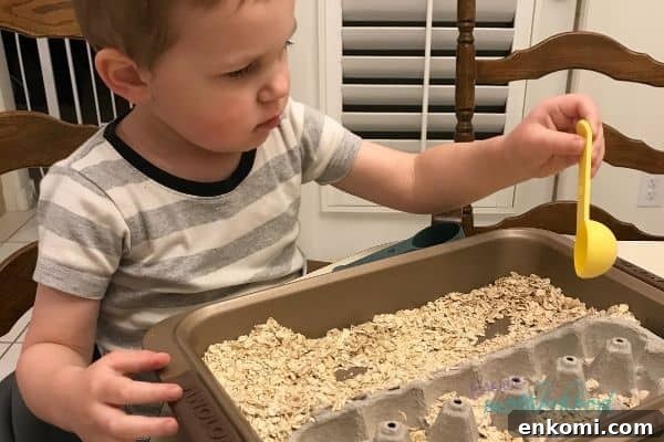Child at a table with an easy sensory bin comprised of a metal baking pan, the bottom half of an egg carton, oats, and plastic measuring utensils, one of the fun and easy indoor preschool activities in the list.