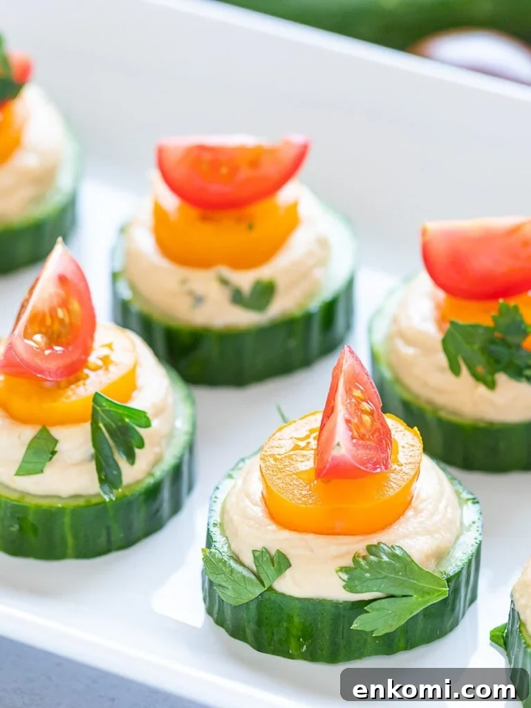 vegan cucumber hummus bites with red and orange cherry tomatoes on a white plate