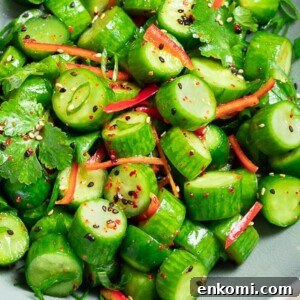Spicy Asian cucumber salad with herbs and red pepper in a blue bowl next to garlic and chopsticks