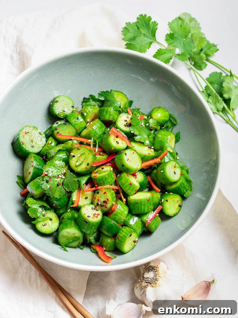 Spicy Asian Cucumber Salad Recipe with Chili-Sesame Dressing 4 Spicy Asian cucumber salad with herbs and red pepper in a blue bowl next to garlic and chopsticks