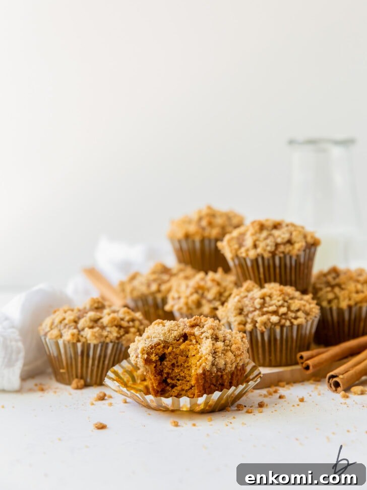 pumpkin muffin with streusel on open paper liner with more muffins piled in the background