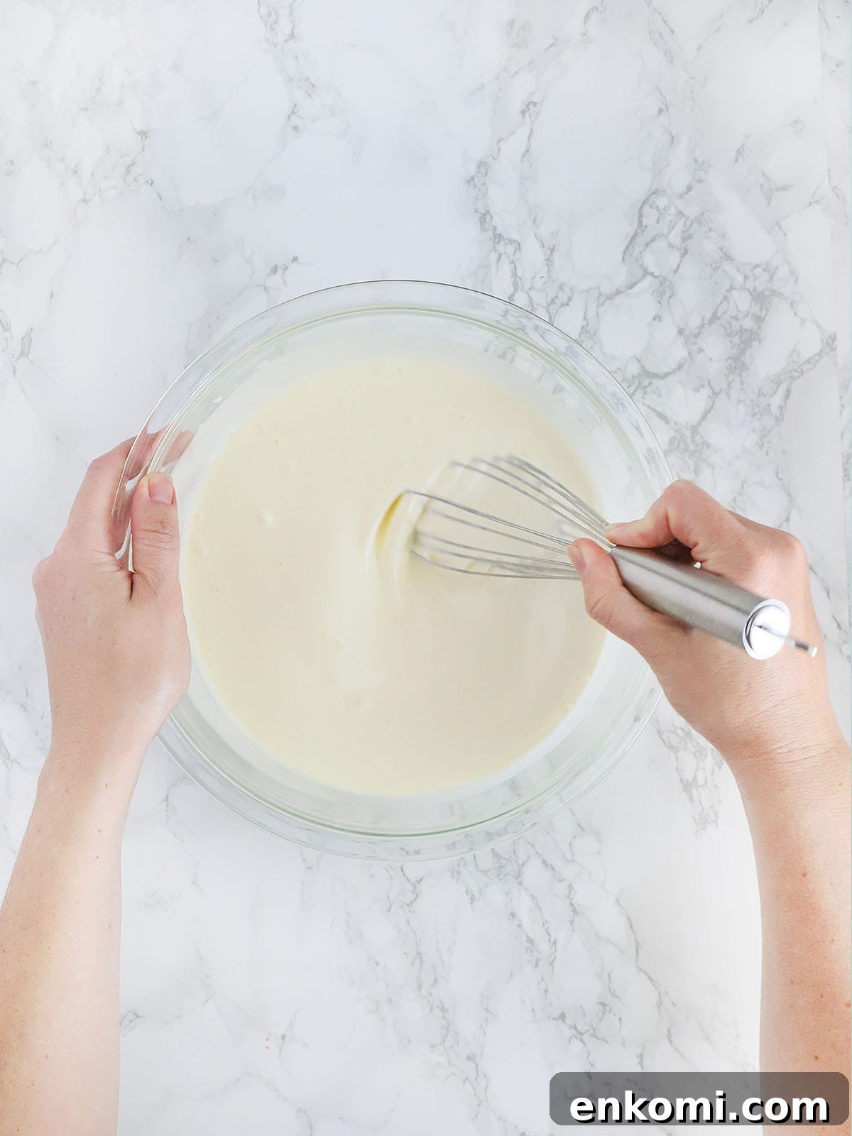 hands whisking together mayonnaise and buttermilk in a glass bowl