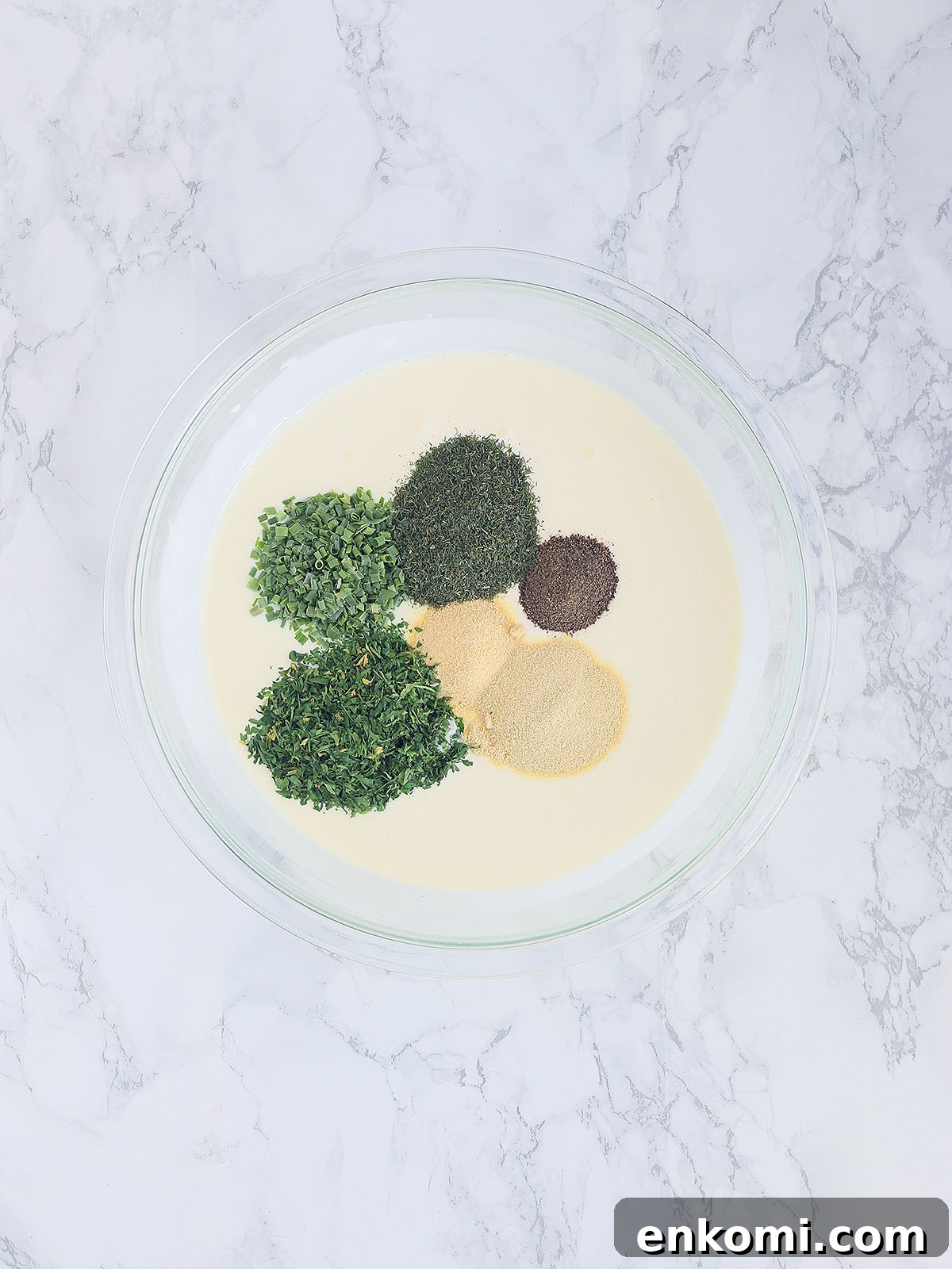 piles of herbs and spices resting on top of a bowl of combined mayonnaise and buttermilk