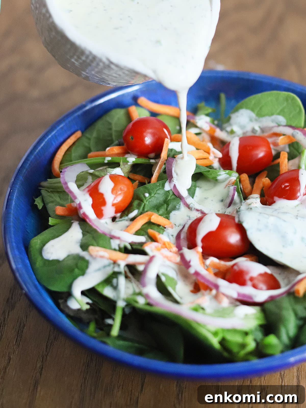 pouring buttermilk ranch dressing over a salad in a blue bowl
