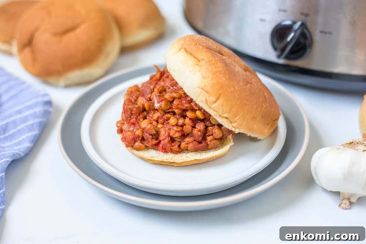 Vegan Sloppy Joe made with lentils served on a bun on a plate with the crockpot in the background.