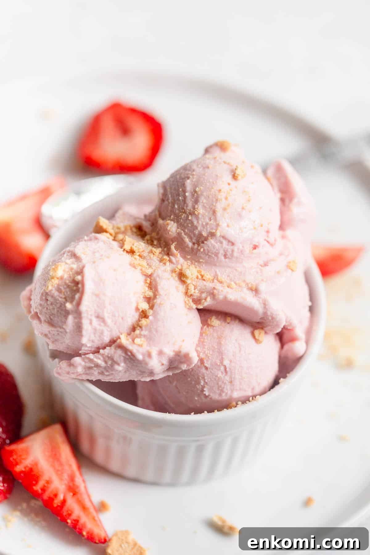 Strawberry Cottage Cheese Ice Cream with crushed graham crackers sprinkled on top in a white bowl with fresh sliced strawberries in the background.