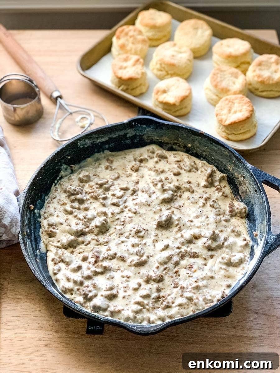 Creamy Sausage Gravy for Biscuits: Homemade Southern Recipe 2 a cast iron skillet of gravy sausage with a pan of biscuits in the background.