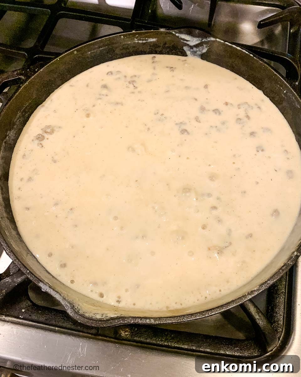 Creamy Sausage Gravy for Biscuits: Homemade Southern Recipe 6 a cast iron skillet of sausage and milk simmering on the stove.