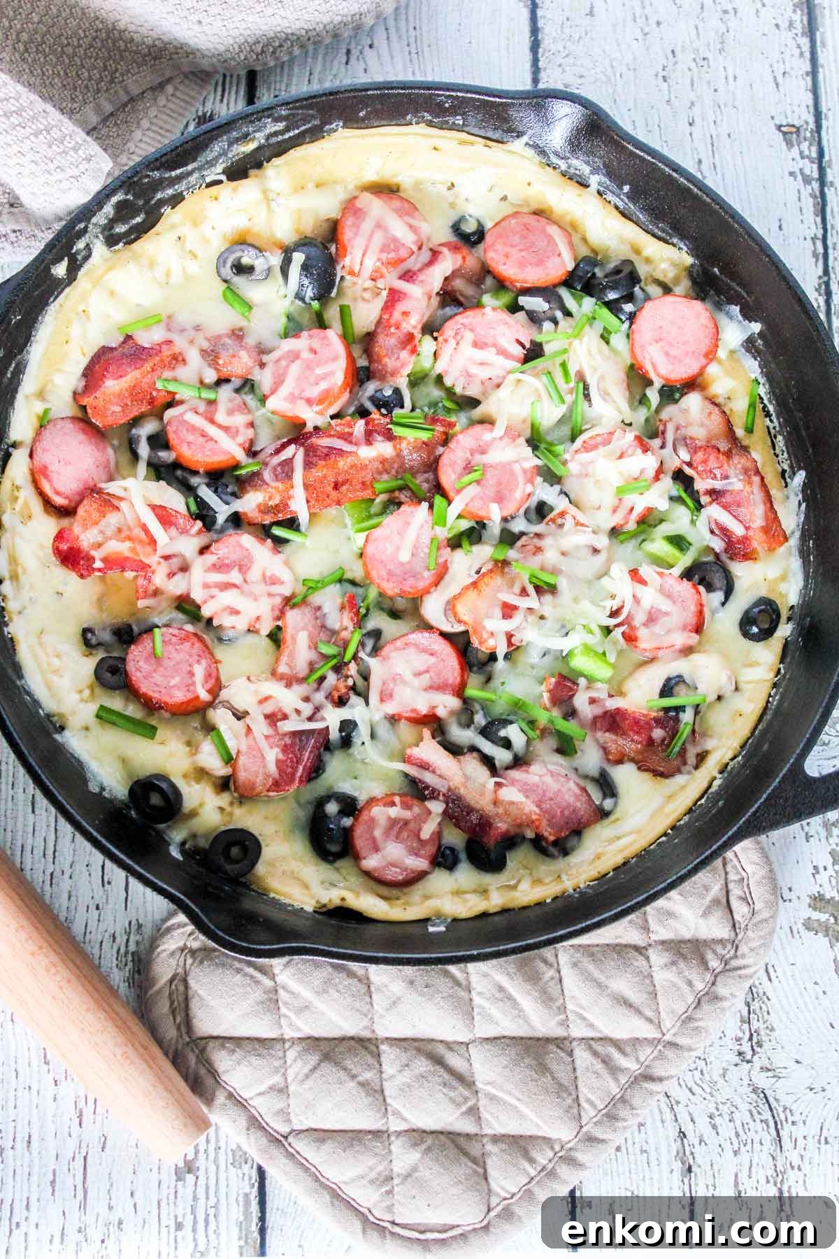 Loaded White Pesto Pizza in a Cast Iron Skillet: Crispy & Cheesy 2 Photo of Loaded White Pesto Pizza in a skillet with a roller and pot holder