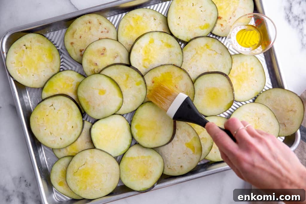 Greek-Style Grilled Eggplant Salad with Simple Grilling Tips 4 Process shot showing a hand brushing olive oil onto eggplant slices.