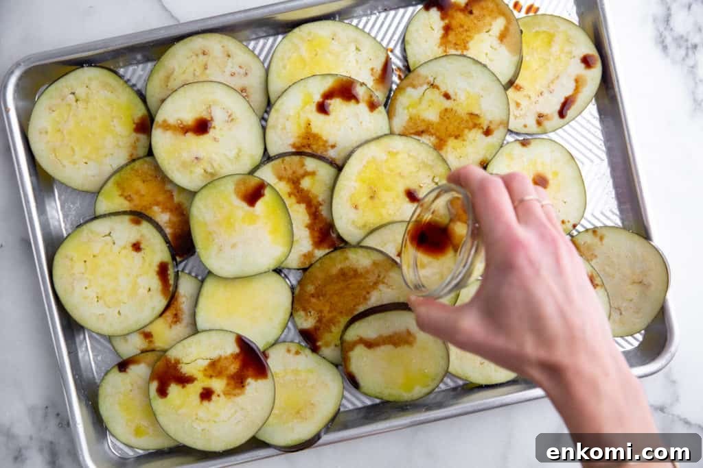 Greek-Style Grilled Eggplant Salad with Simple Grilling Tips 5 Process shot showing a hand drizzling balsamic vinegar over eggplant slices on a sheet pan.