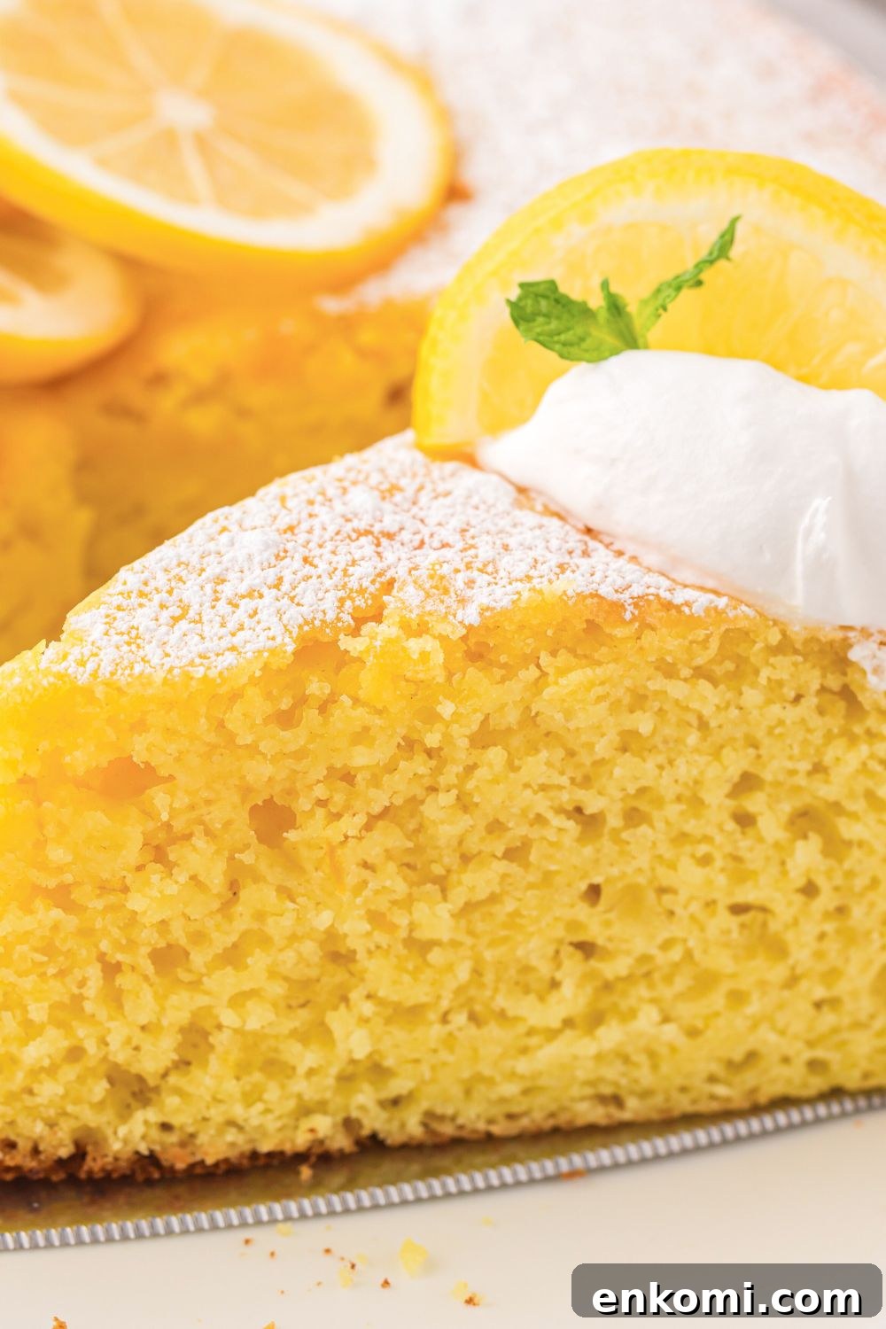 close up of Italian Lemon Ricotta Cake on plate with lemons sliced behind it on table 