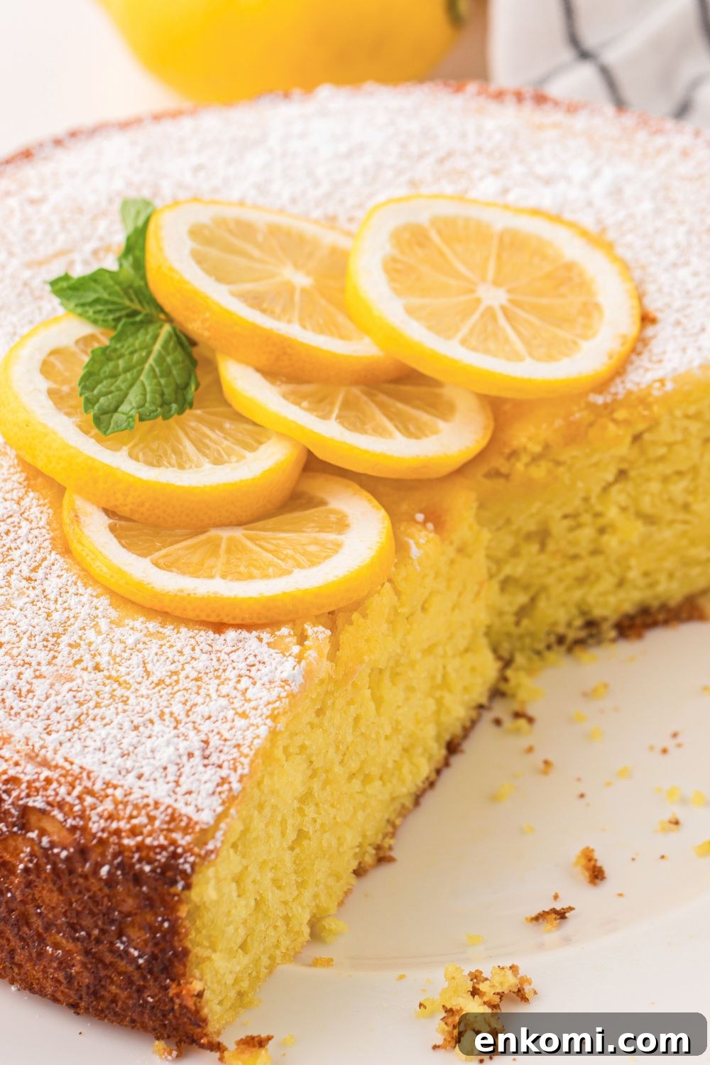 Italian Lemon Ricotta Cake on table with a few slices taken out of it and lemon wedges on top 