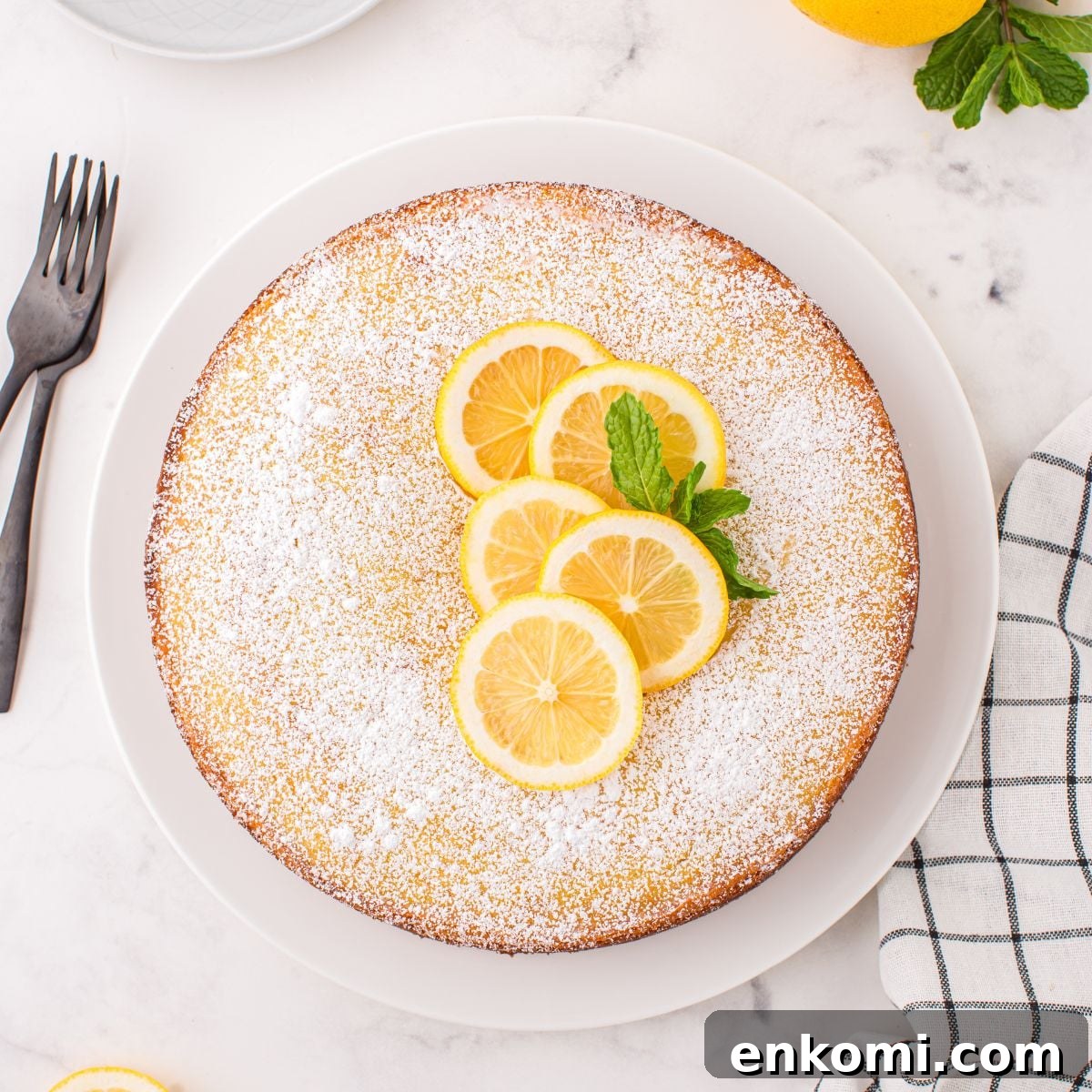 Italian Lemon Ricotta Cake on table with some fresh lemons on top with some mint leaves to side 