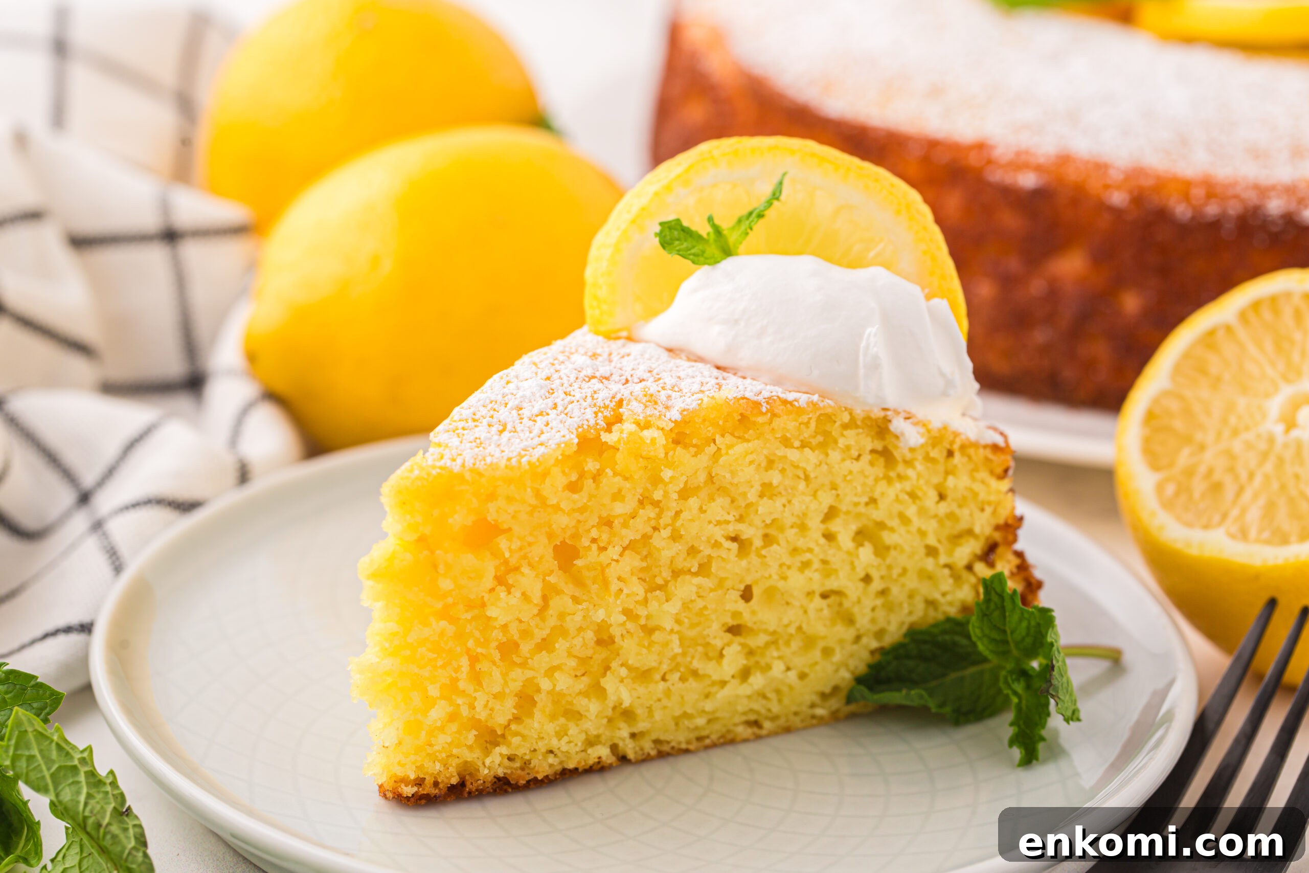slice of Italian Lemon Ricotta Cake on plate with whole lemons behind it on table and the rest of the cake behind it on table 