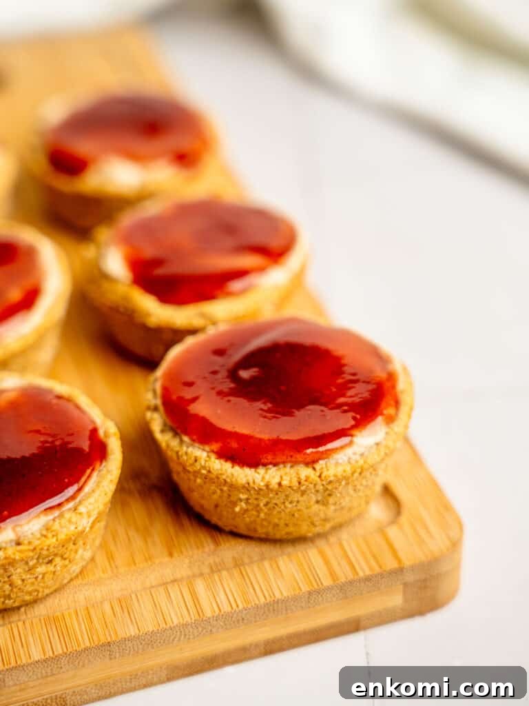 High-Protein Mini Cheesecakes: Low-Calorie Dessert Recipes 2 Mini protein cheesecakes with strawberry jam on a wooden chopping board.
