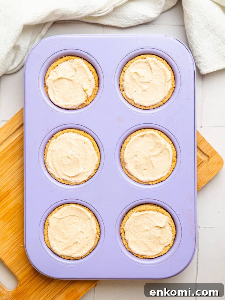 High-Protein Mini Cheesecakes: Low-Calorie Dessert Recipes 8 Mini cheesecake crusts filled with protein cheesecake filling in a muffin tray.