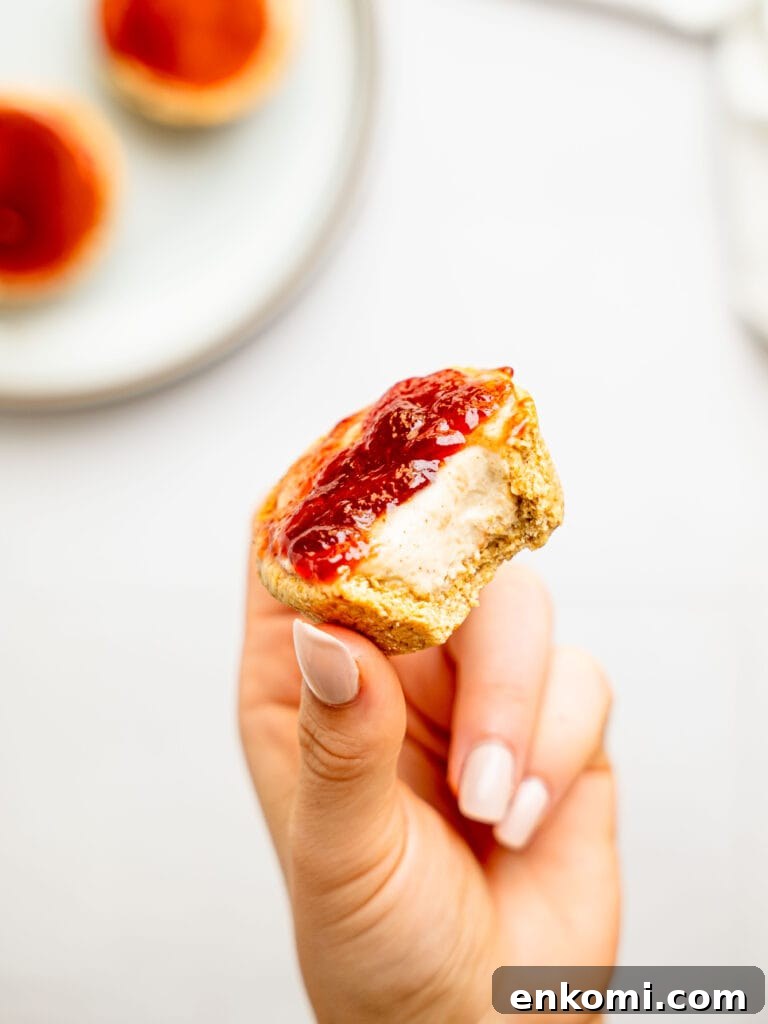 High-Protein Mini Cheesecakes: Low-Calorie Dessert Recipes 10 Hand holding a half-eaten mini protein cheesecake with strawberry jam.