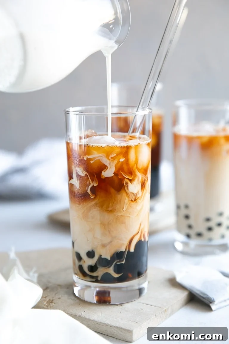How to Make Authentic Bubble Tea at Home: Tapioca Pearl Recipe 2 Pouring milk into a tall glass filled with cooked tapioca pearls, strong black tea, and ice.