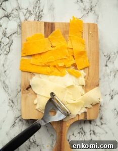 overhead shot of shaved cheese on wooden chopping board with potato peeler